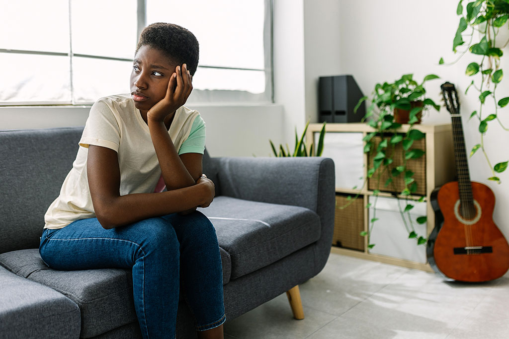 A Black Woman Sitting On A Couch Wondering What Are The Risks With Abortion.