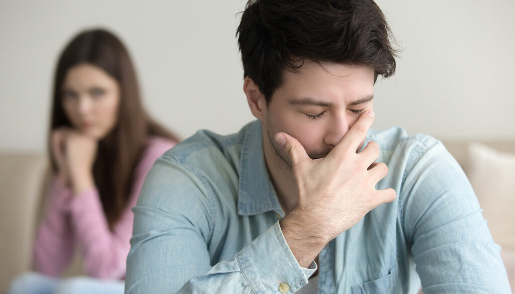 Young Man Stressed With His Hand Over His Face With His Girlfriend Sitting Behind Him Unplanned Pregnancy Advice for Men